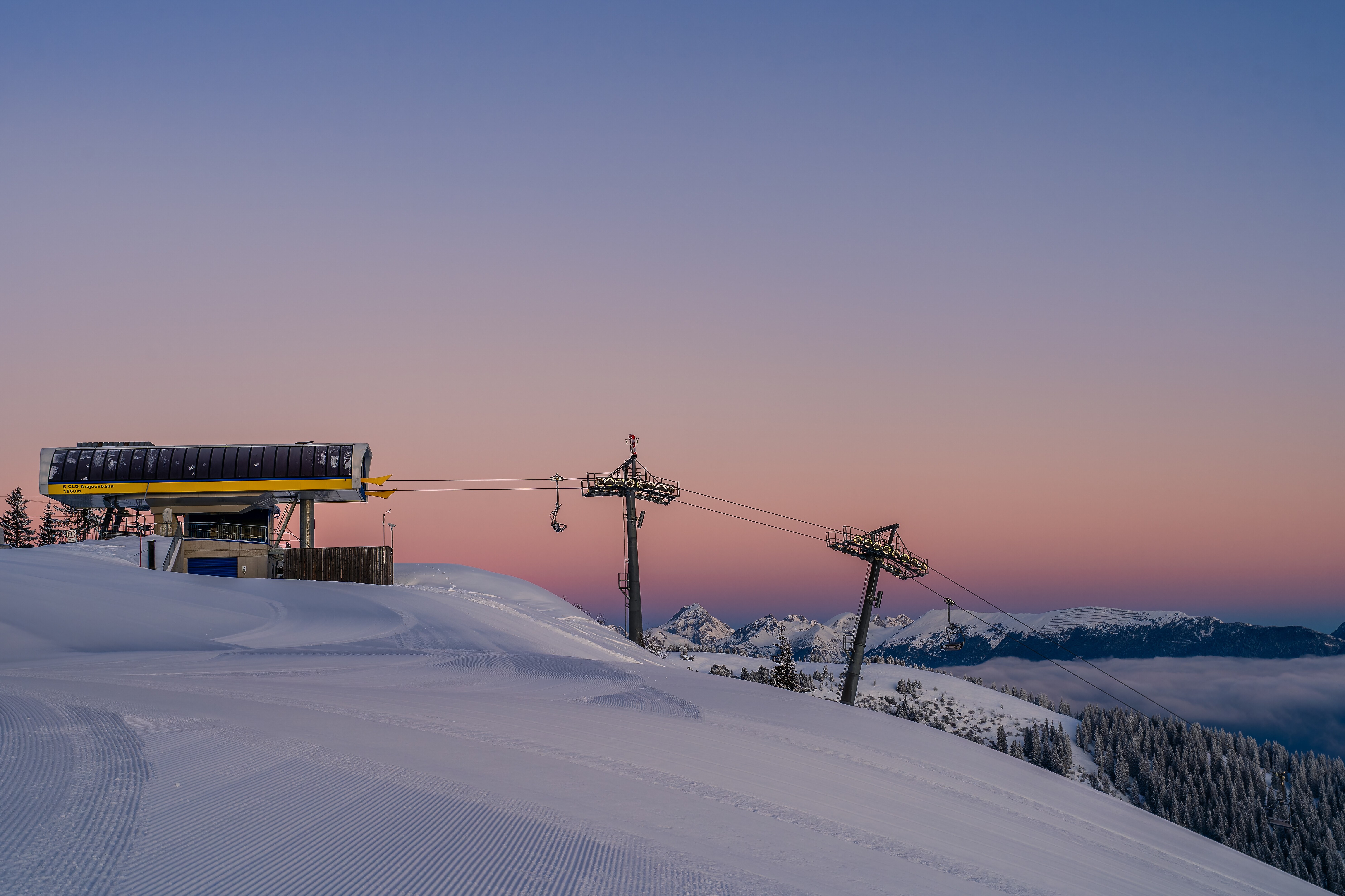 Groomed ski slope on the Onkeljoch with a lift and snow-covered mountains in the morning light